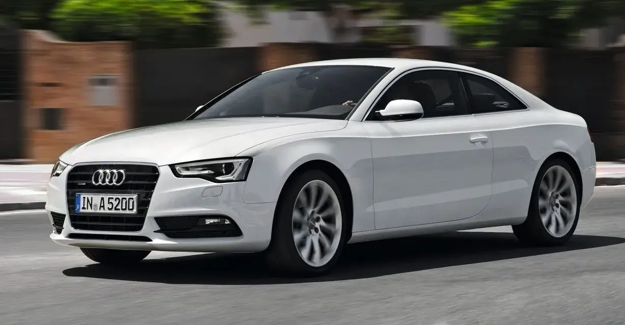Białe Audi A5 Coupe pędzi po drodze, jego sylwetka jest dynamiczna i elegancka.