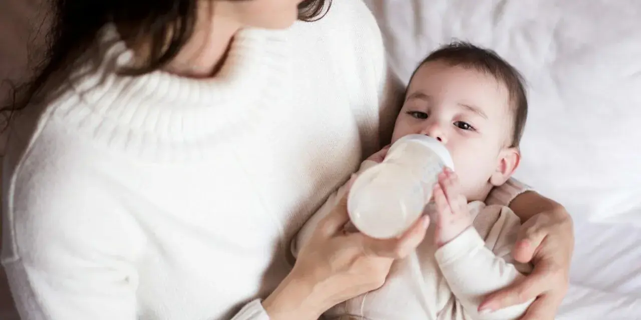 Mama karmi butelką dziecko, które właśnie pije mleko. Ważne jest, ile mleka powinien jeść noworodek.