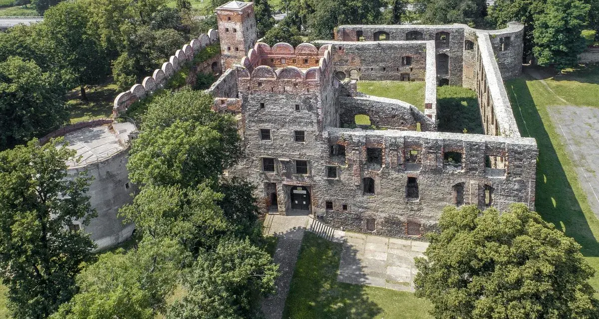 Ruiny zamku w Ząbkowicach Śląskich, z charakterystyczną basztą i murami obronnymi, otoczone zielenią.