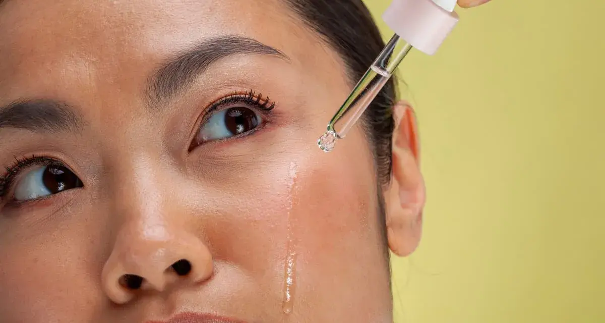Kropla serum z pipetki spada na policzek kobiety. To może być retinol, który co to jest i jak działa, warto sprawdzić.