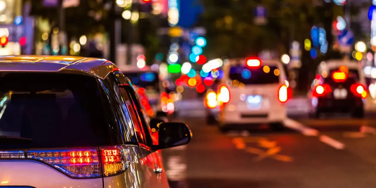 Luci sfocate e colorate in una strada trafficata di notte, come vedono i miopi le luci. Un'auto argentata in primo piano.