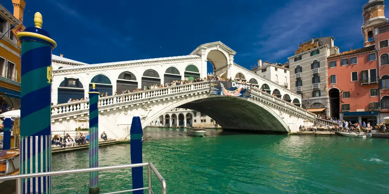 Ponte di Rialto, un'icona della storia veneziana, con le sue botteghe e la folla che lo attraversa, si specchia nelle acque verdi del Canal Grande.