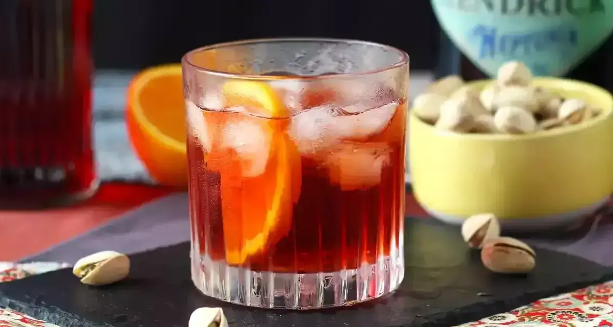Przepis na Negroni Sbagliato: orzeźwiający drink z pomarańczą i lodem, obok miseczka pistacji.