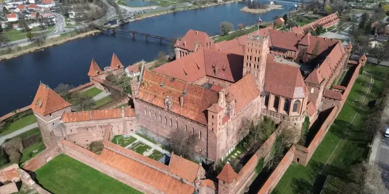 Potężny zamek z czerwonej cegły, największy zamek w Europie, otoczony murami obronnymi, nad rzeką.