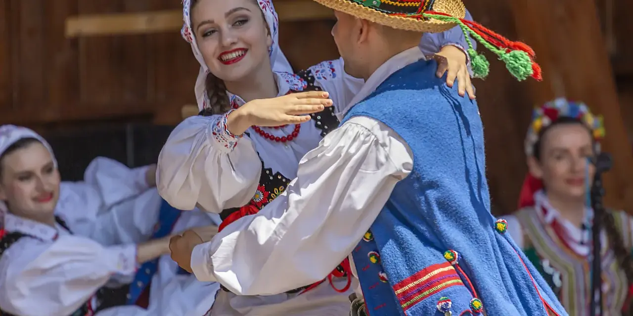Uśmiechnięta para w tradycyjnych strojach tańczy do skocznych piosenek ludowych.