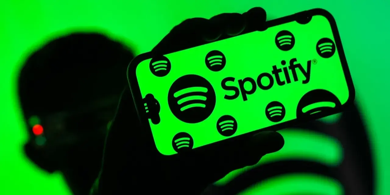 Dłoń trzyma smartfon z zielonym ekranem, na którym widnieje logo Spotify. Użytkownik cieszy się doskonałą spotify jakość dźwięku.