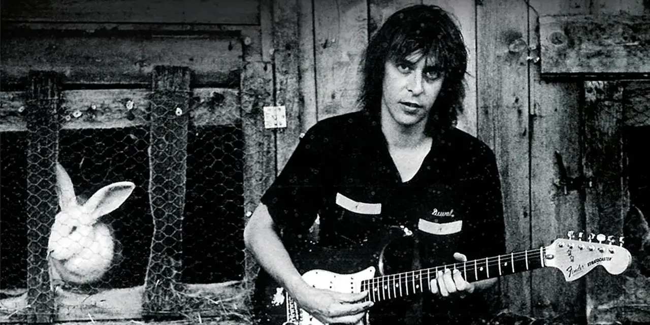Ein Mann mit Gitarre, im Hintergrund ein Hase im Käfig. Ein Bild, das an den **titel von Rio Reiser** erinnert.
