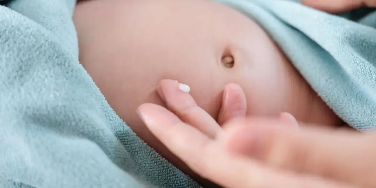 Delikatna pielęgnacja brzuszka niemowlaka. Kropelka kremu na palcu, gotowa do naniesienia na pępek, gdzie może występować przepuklina pępkowa.