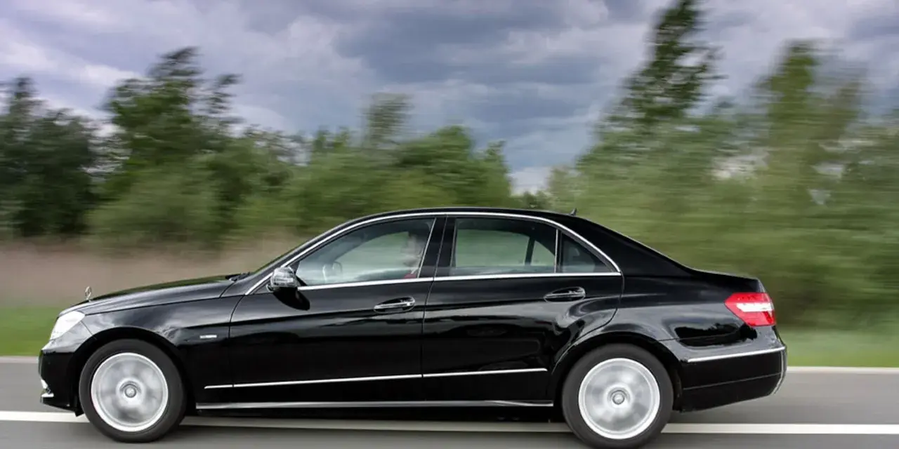 Czarny Mercedes E350 pędzi po drodze, mijając rozmyte zielone drzewa.