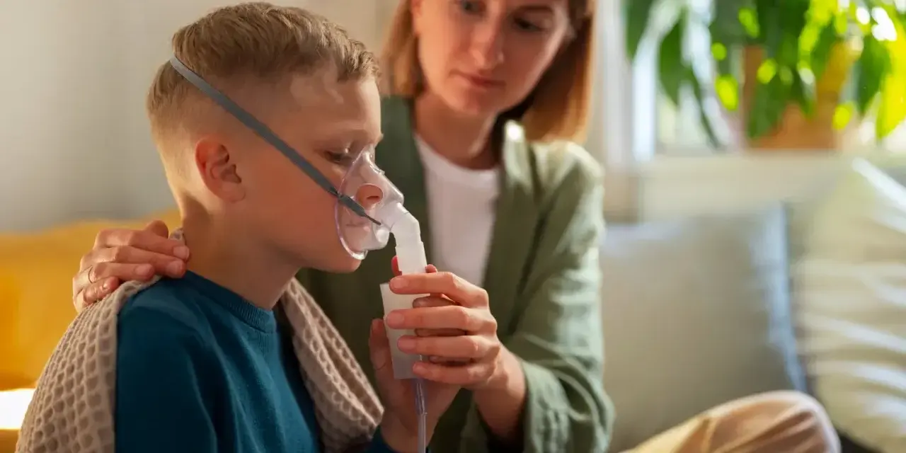 Chłopiec z maską nebulizatora, wspierany przez matkę. Dbałość o zdrowie dziecka z astmą wczesnodziecięcą.