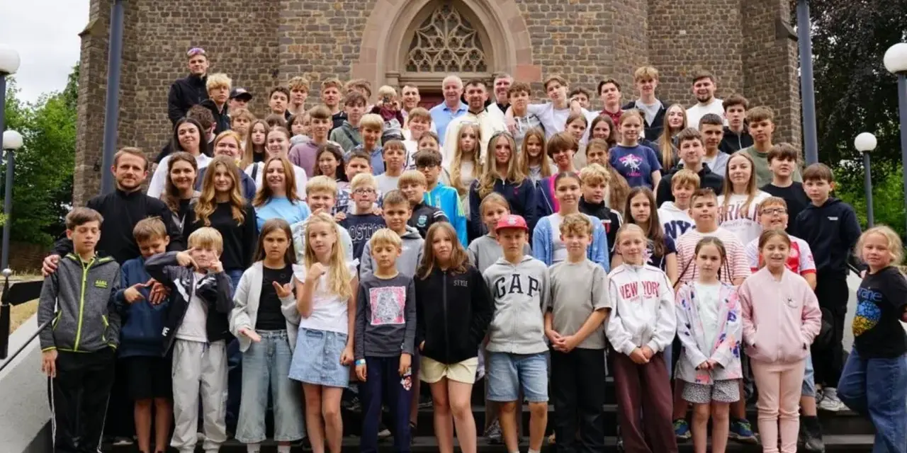 Große Gruppe von Kindern und Jugendlichen vor einer Kirche, die an einem christlichen Ferienlager teilnehmen.