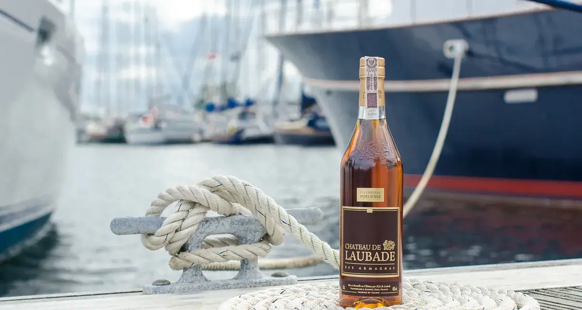 Butelka Bas Armagnac Chateau de Laubade stoi na tle jachtów. To doskonały trunek, jeśli zastanawiasz się, armaniak co to.
