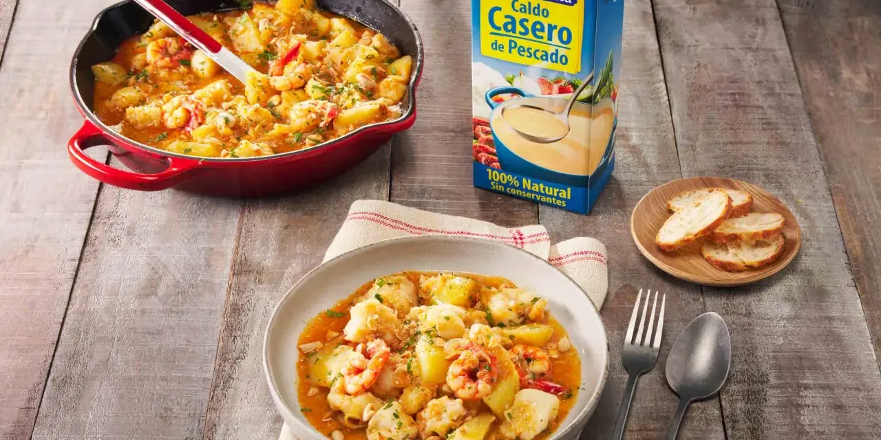Un delicioso rape a la marinera, con patatas y gambas, servido en una cazuela roja y un plato.