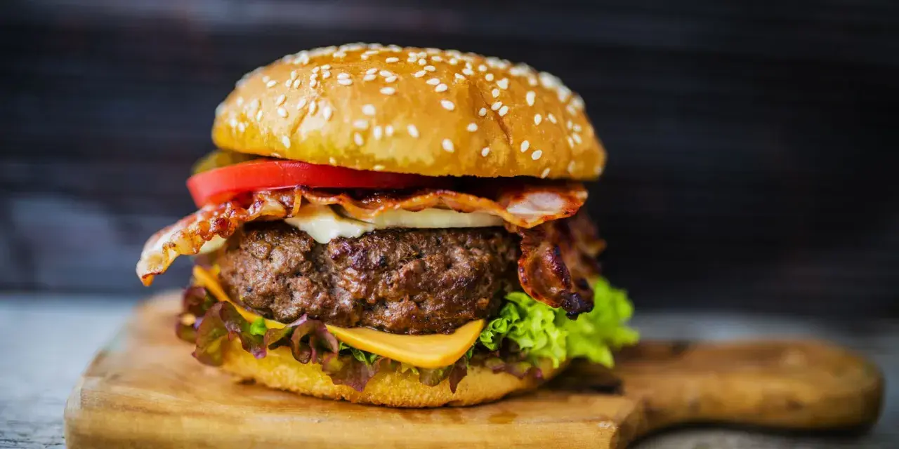 Hamburger di carne succulento con bacon croccante, formaggio fuso, pomodoro e lattuga su panino ai semi di sesamo.
