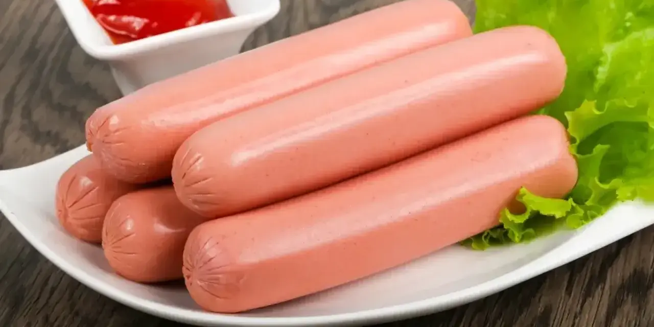 Kilka parówek na talerzu z sałatą i ketchupem. Idealne do szybkiego obiadu, dowiedz się, jak ugotować parówki.