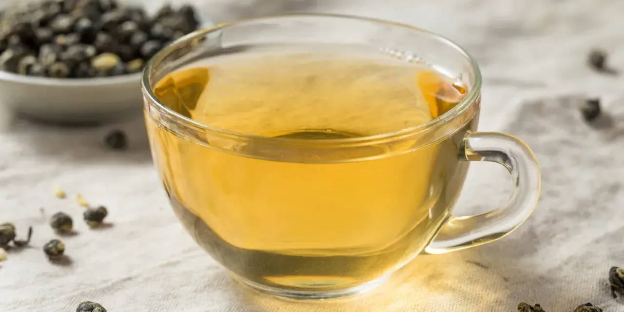 Zaparzona herbata oolong w szklance, obok miseczka z suszonymi liśćmi. Odkryj niezwykłe herbata oolong właściwości.
