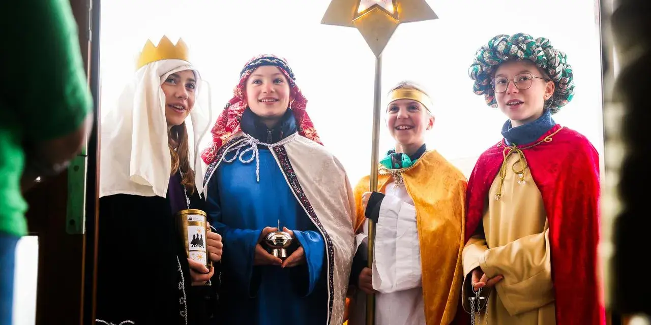 Vier Kinder als Sternsinger evangelisch verkleidet, mit Stern und Spendenbüchse, stehen vor einer Tür.