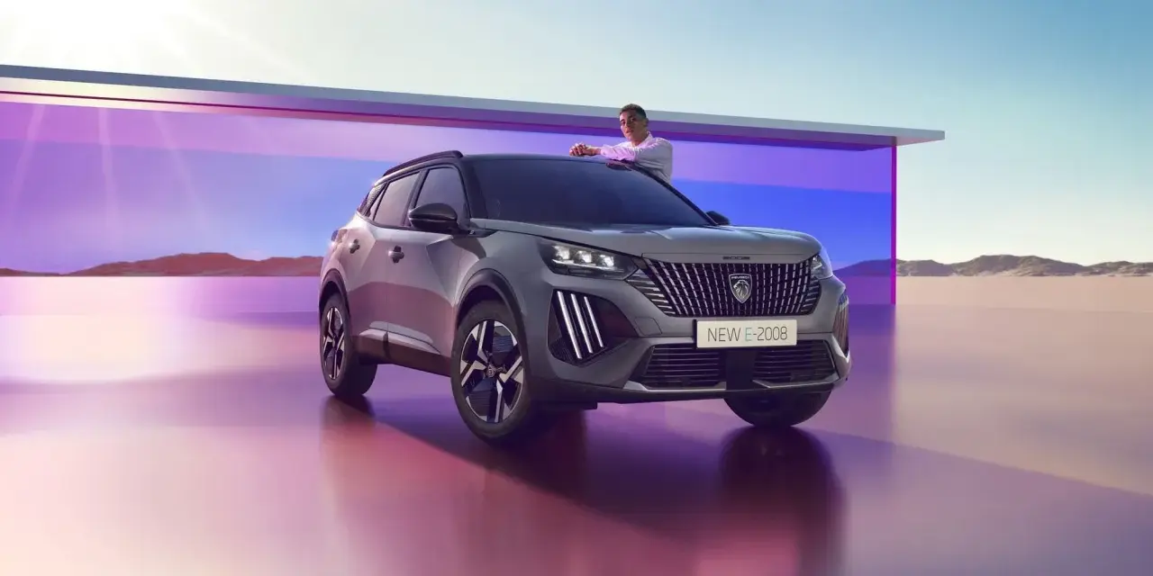 Mężczyzna opiera się o maskę nowego Peugeot E-2008, stylowego peugeot suv, na tle futurystycznej architektury i pustynnego krajobrazu.