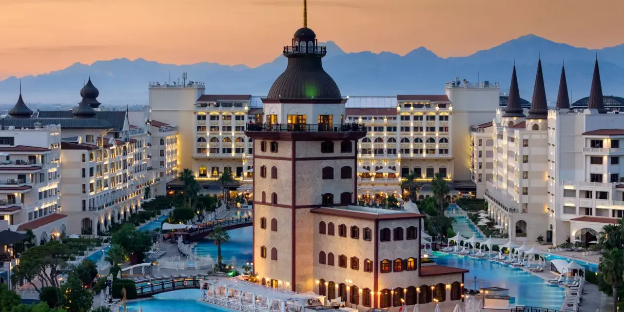 Luksusowy hotel z basenami i wieżą, idealny na wakacje all inclusive w Turcji. Góry w tle.
