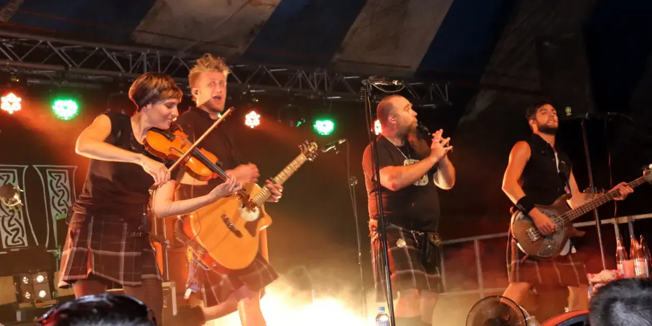 Un groupe celtique français sur scène, avec violon, guitare et basse. Les musiciens portent des kilts, créant une ambiance festive.