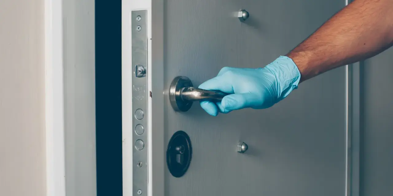Ręka w niebieskiej rękawiczce chwyta klamkę drzwi, przygotowując się do budowy zamka w drzwiach.
