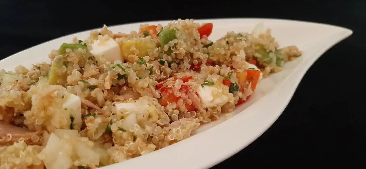 Salade colorée de quinoa avec des dés de feta, avocat, tomates et persil, servie dans un plat blanc.
