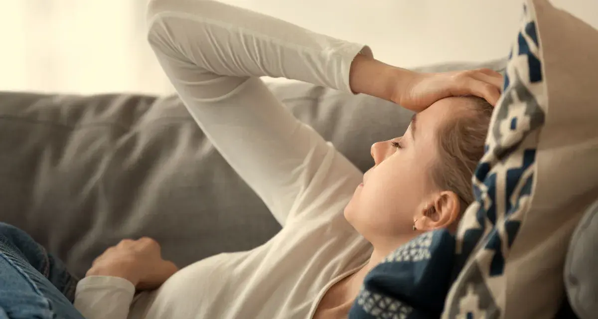 En kvinna med handen mot pannan, utmattad. Kan vara tecken på b12-brist stress.