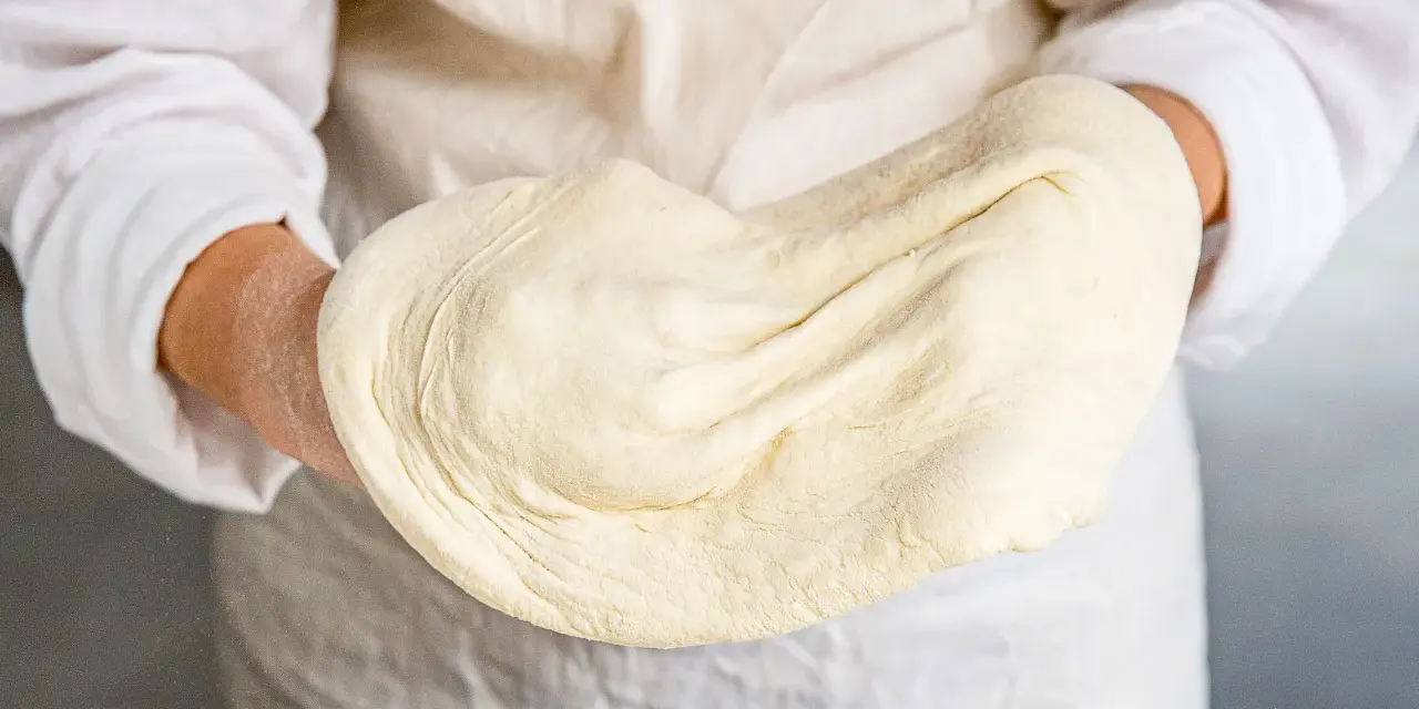 Hände halten geschmeidigen pizzateig, original rezept von einem italienischen gastronomen. Perfekt für authentische Pizza.