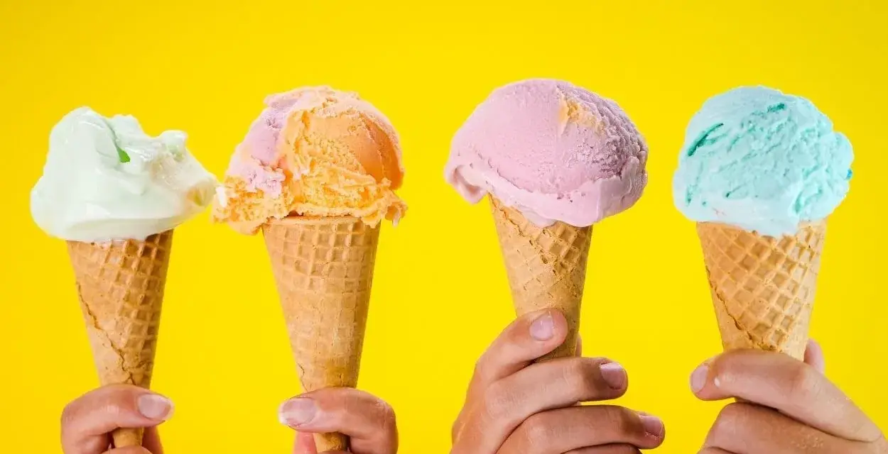 Vier Hände halten bunte Speiseeiswaffeln vor gelbem Hintergrund. Die ideale Temperatur für Speiseeis.