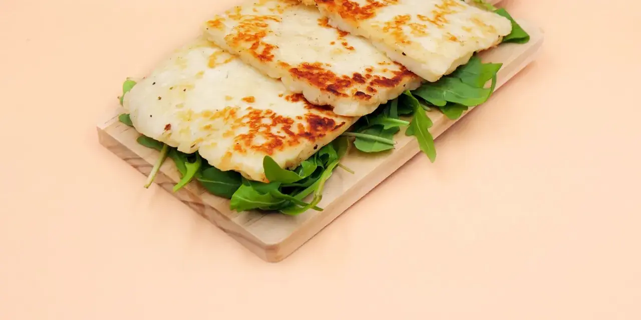 Trzy złociste plastry sera halloumi na desce z rukolą. Czy w ciąży można jeść ser halloumi? Tak, jeśli jest pasteryzowany.