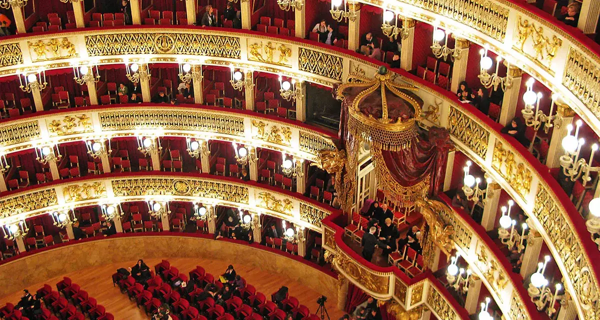 Elegancka loża w teatrze, z czerwonymi aksamitnymi siedzeniami i złotymi zdobieniami, czeka na widzów.