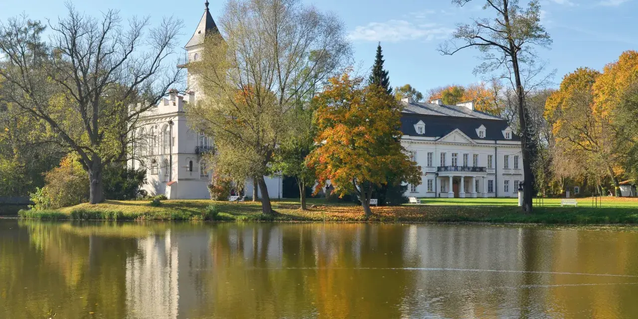 Pałac w jesiennej scenerii nad jeziorem, część Bolimowskiego Parku Krajobrazowego. Kaczka pływa po wodzie.
