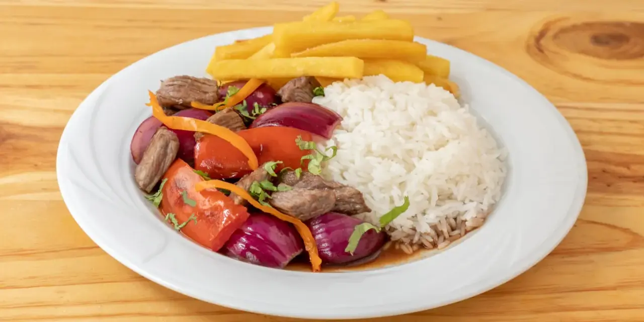 Lomo saltado con arroz blanco, papas fritas, carne, cebolla roja y tomate. Un plato peruano delicioso.
