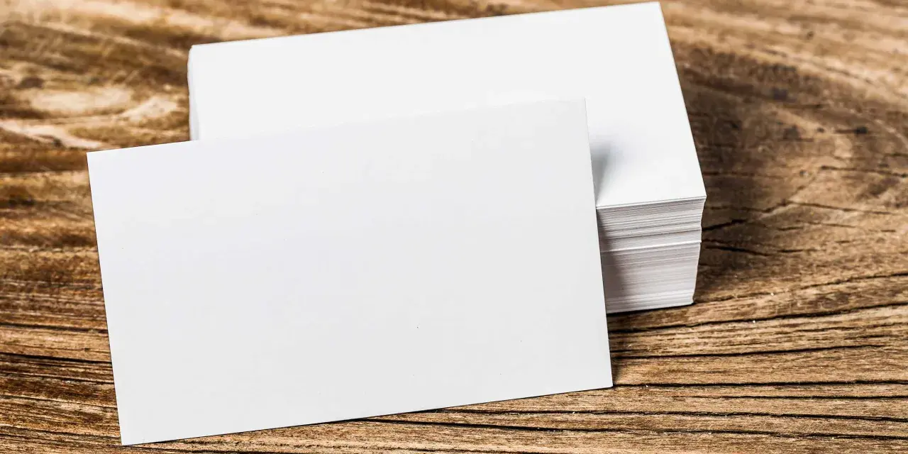 Pila de tarjetas de visita blancas sobre madera. Se aprecian los diferentes grosores de papel en la pila.