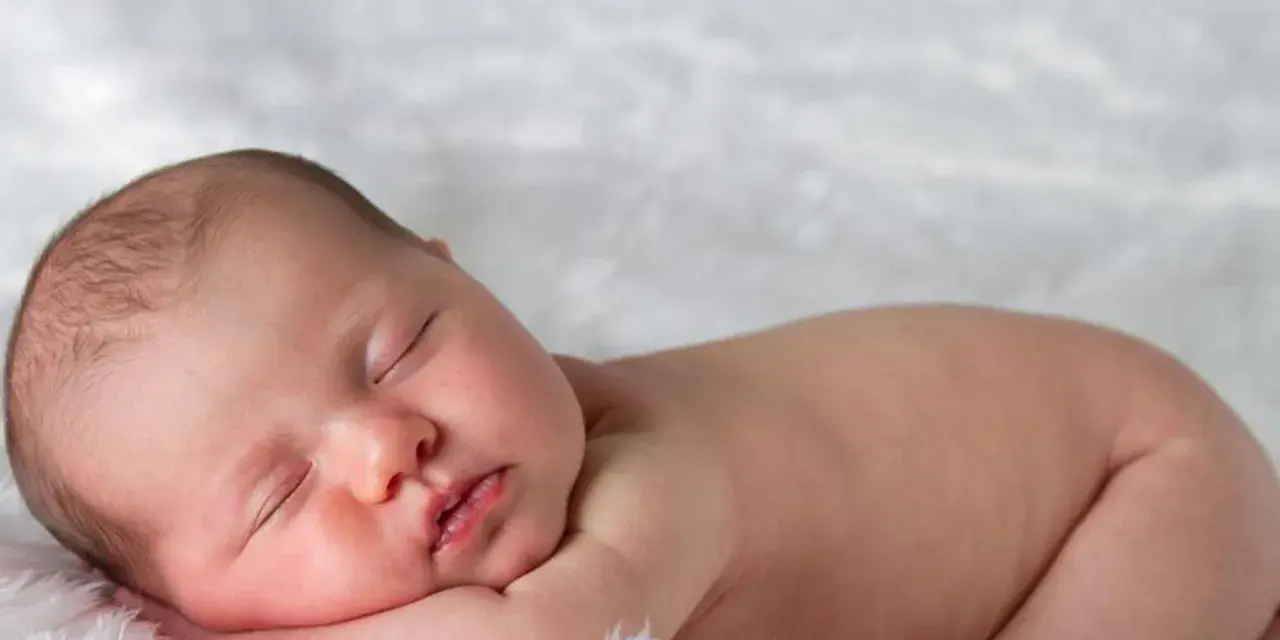 Śpiące, 3 miesięczne dziecko z delikatnymi włoskami, wtulone w miękkie futerko.