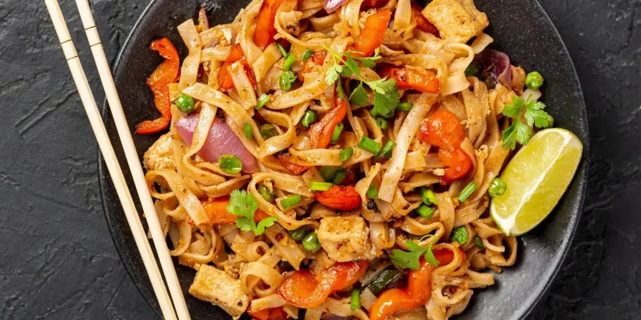 Pyszny pad thai z kurczakiem, warzywami i makaronem ryżowym, udekorowany kolendrą i ćwiartką limonki.