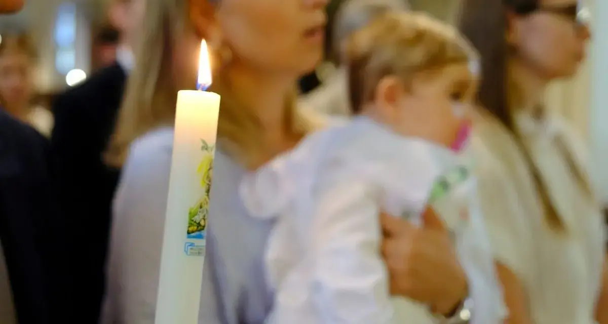 Chrzest dziecka. Czy świadek chrztu musi mieć zaświadczenie? Płonąca świeca chrzcielna w dłoniach.