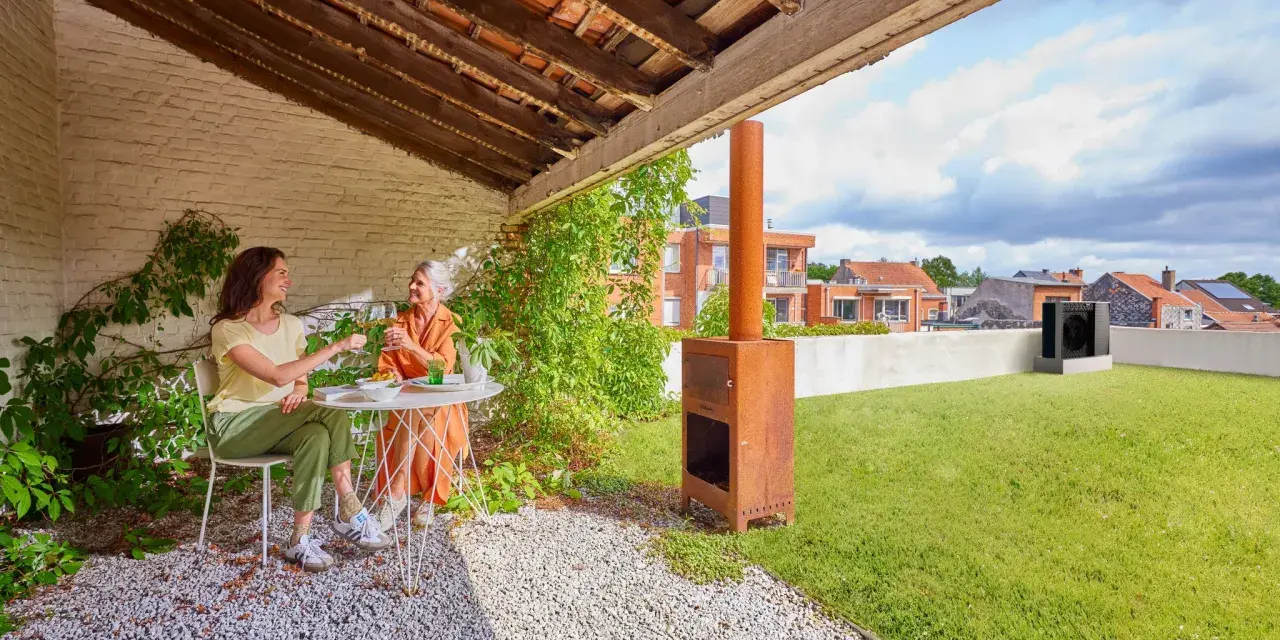 Due donne brindano su un terrazzo con prato. Sullo sfondo, una pompa di calore sul tetto.