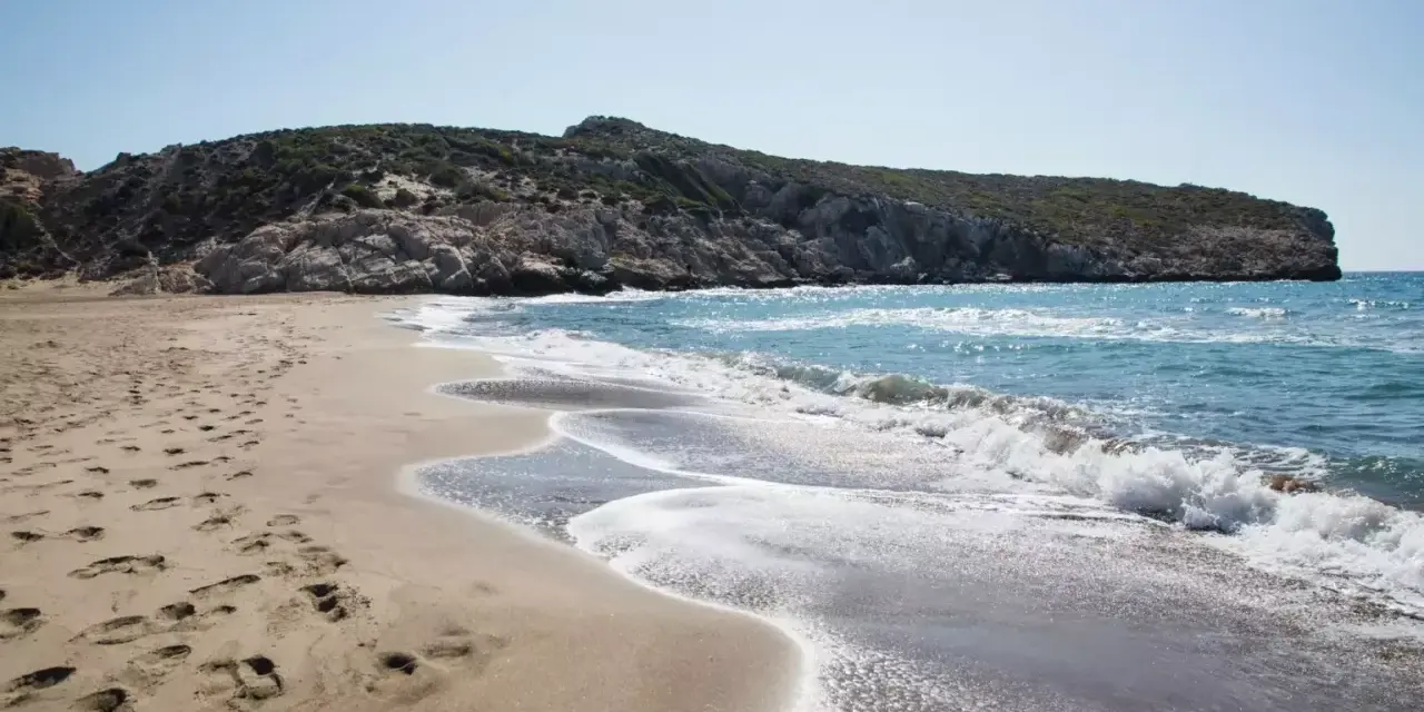 Piękne turcja plaże z piaszczystym brzegiem i skalistym wzgórzem w tle. Fale delikatnie rozbijają się o brzeg.