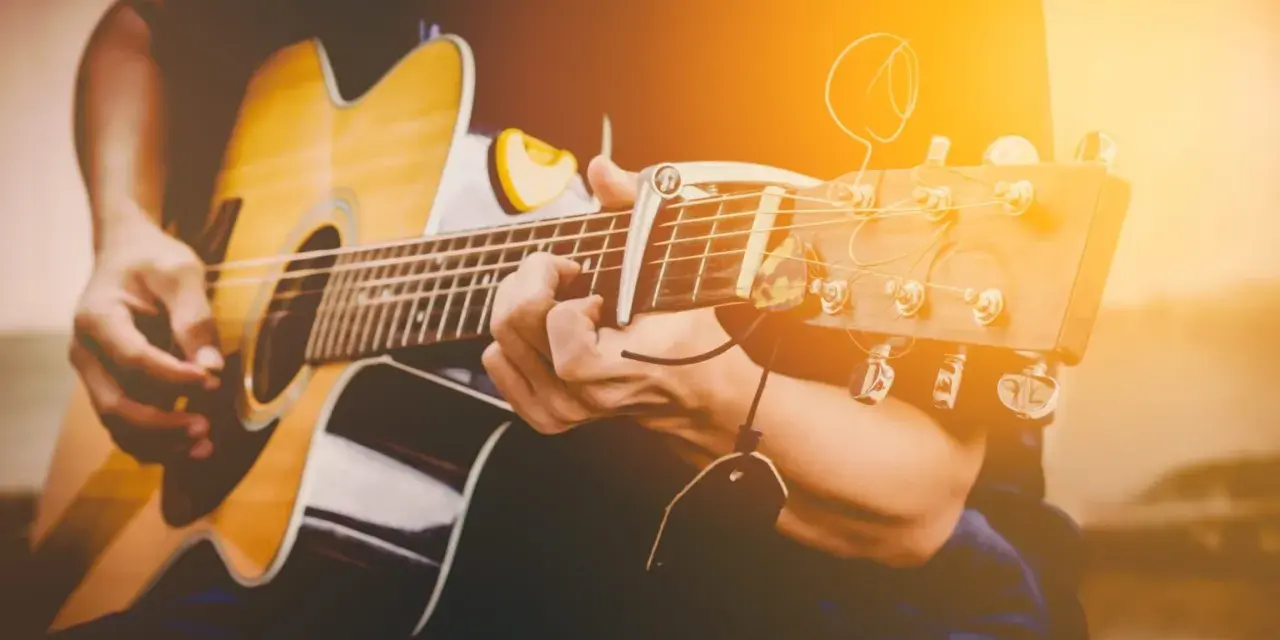 Osoba gra na gitarze akustycznej. Zastanawiasz się, ile trwa nauka gry na gitarze? To zależy od Ciebie!