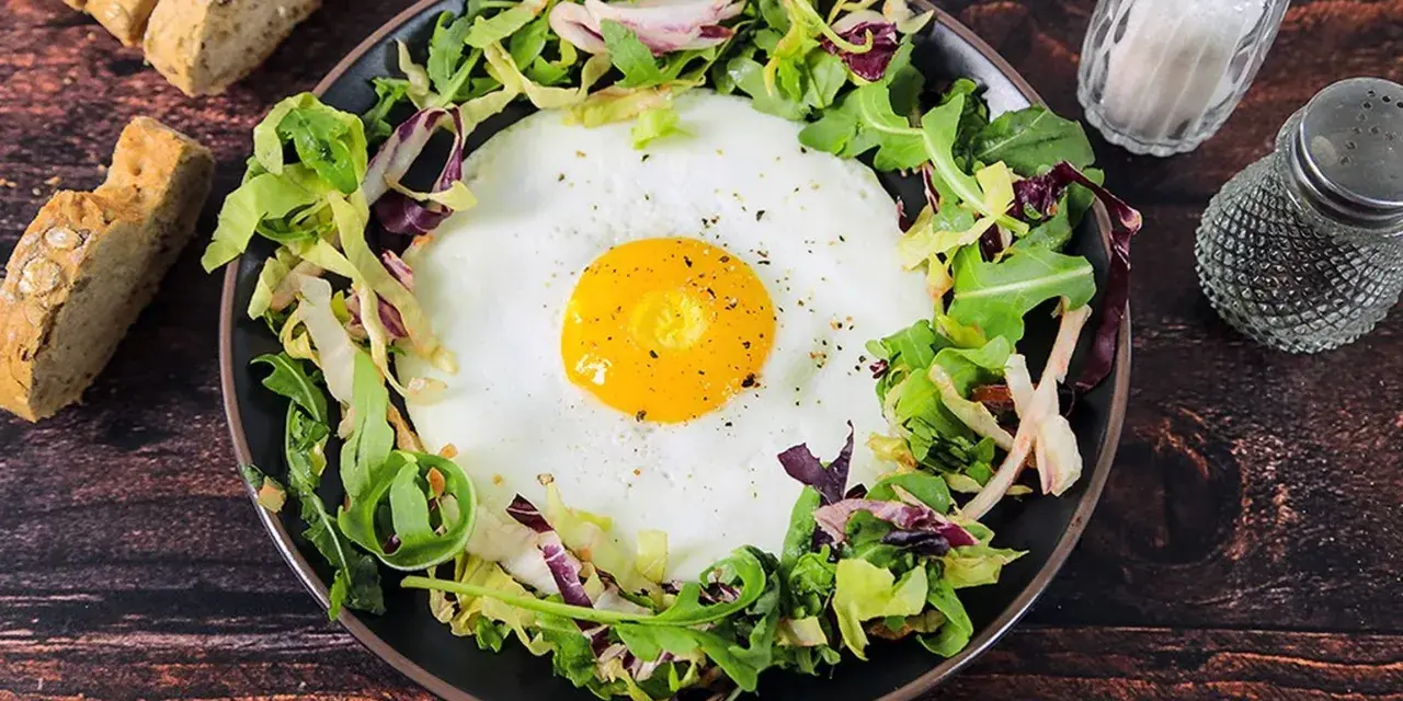 Un uovo occhio di bue su un letto di insalata mista, servito con pane integrale e condimenti.