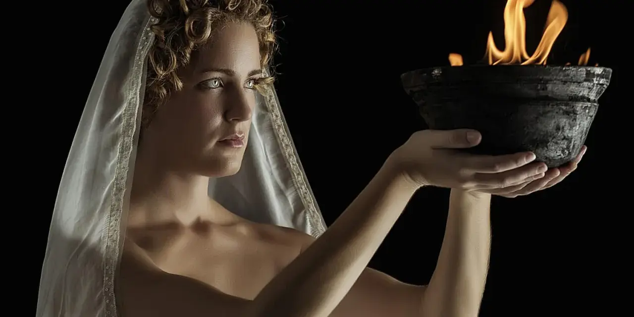 A woman with curly hair and a veil, embodying Hestia goddess, holds a bowl with a sacred flame.