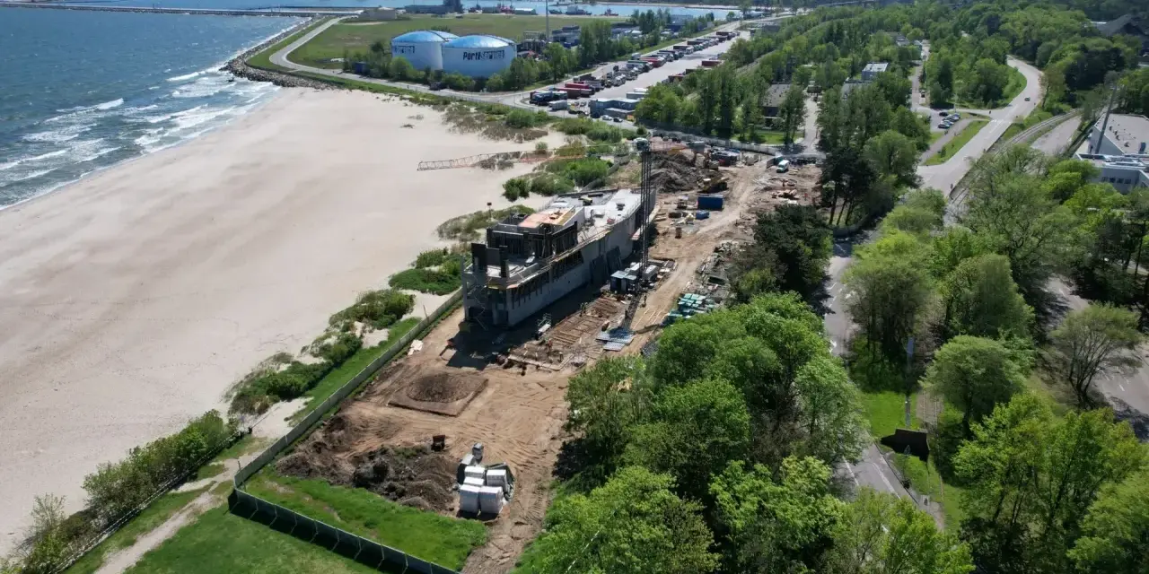 Gdańsk deptak nad morzem w budowie. Nowoczesny obiekt powstaje tuż przy plaży, w tle port i przemysłowe krajobrazy.