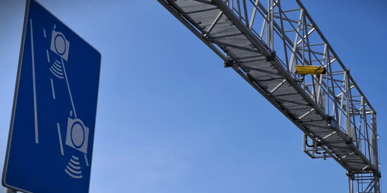 Niebieski znak informuje o odcinkowym pomiarze prędkości S7. Nad drogą widać konstrukcję z żółtą kamerą.