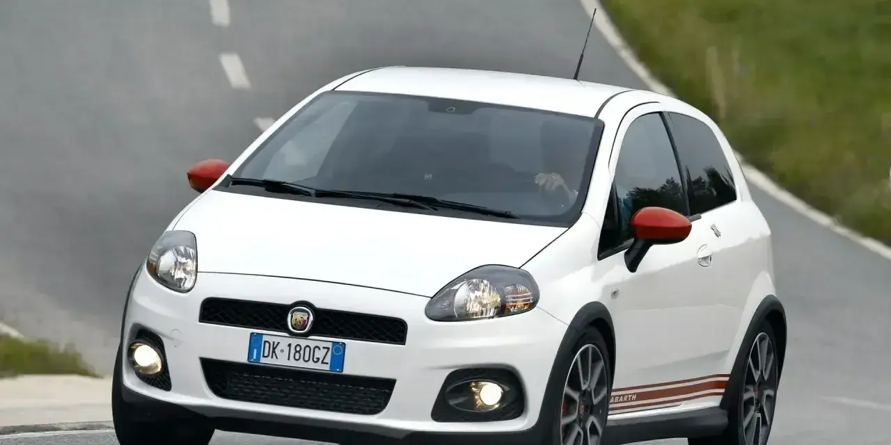 Biały Fiat Punto Evo Abarth z czerwonymi lusterkami pędzi po zakręcie drogi.