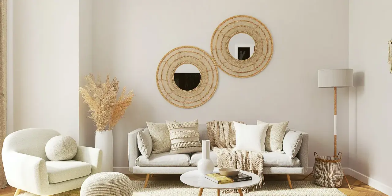 Salotto accogliente con divano grigio, poltrona bianca, tavolino rotondo e specchi decorativi in rattan. Un esempio di come arredare case moderne con stile boho-chic.