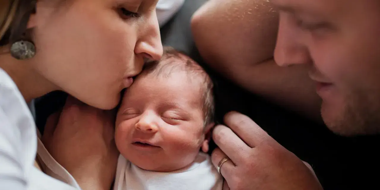 Mutter küsst ihr Neugeborenes, Vater schaut liebevoll zu. Diese Momente sind unbezahlbar, auch nach 1000 Tagen.
