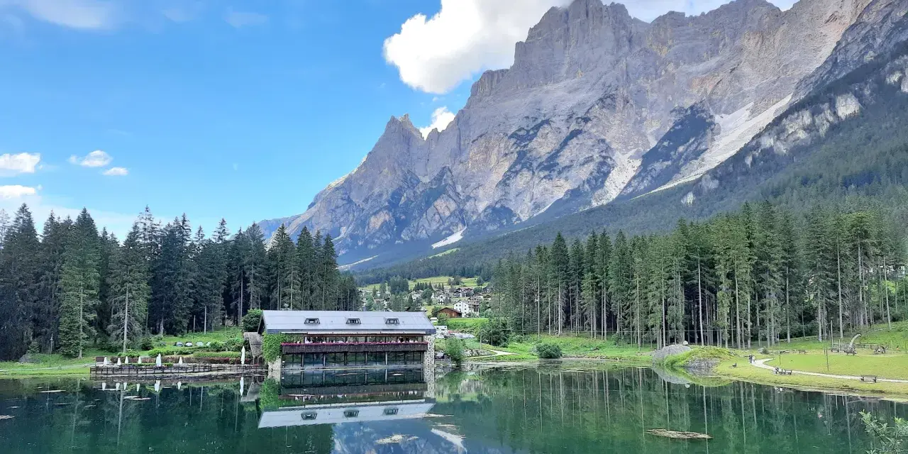 Riflessi alpini sul lago di Mosigo, con un rifugio e montagne imponenti sullo sfondo.