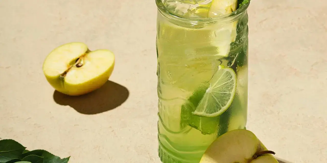 En uppfriskande p2 drink med äpple, lime och mynta. Två halvor av ett grönt äpple ligger bredvid glaset.