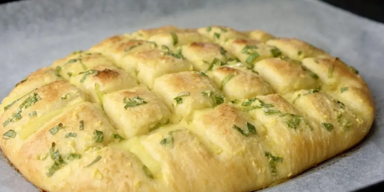 Puszysty chlebek czosnkowy z zieloną cebulką i ciągnącym się serem, podzielony na porcje, gotowy do podania.